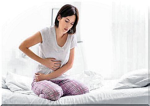 A woman is sitting on a bed with her hands against her stomach