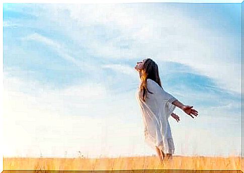 A woman stands in a field with her arms back